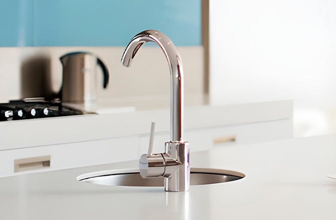 Grifo cromado moderno y fregadero reluciente en una cocina limpia y ordenada.