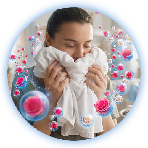 Mujer respirando el aroma de prendas limpias y burbujas de rosas tras lavar ropa en su hogar.