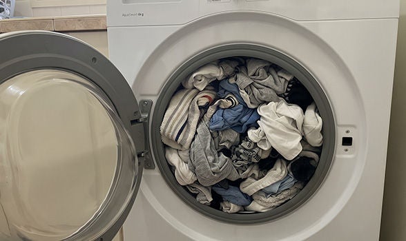Lavadora de carga frontal sobrecargada con demasiada ropa azul, blanca y gris antes de iniciar el lavado.