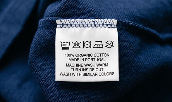 Etiqueta de cuidado de ropa en una prenda azul oscuro con símbolos de lavado y texto indicando 100% algodón orgánico, lavar en máquina con agua tibia y colores similares.