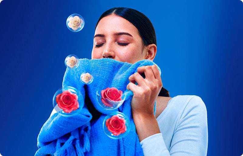 Mujer disfrutando el aroma a rosas de una cobija azul lavada con suavizante Suavitel.