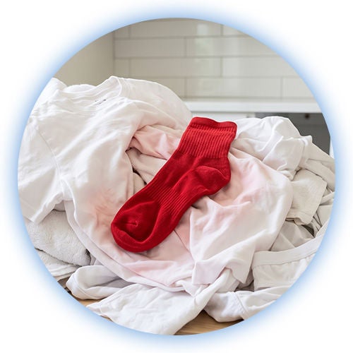 Calcetín rojo sobre ropa blanca, mostrando un error común al no saber cómo separar la ropa para lavar.