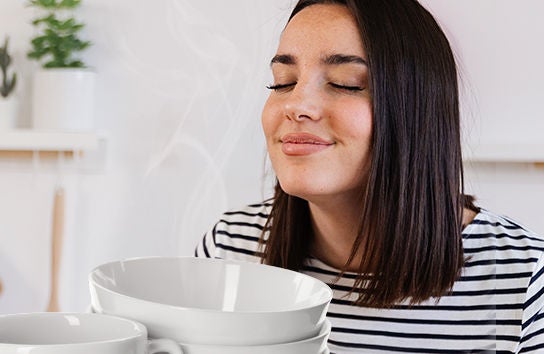 Mujer sonriendo con los ojos cerrados mientras disfruta del aroma limpio de platos recién lavados