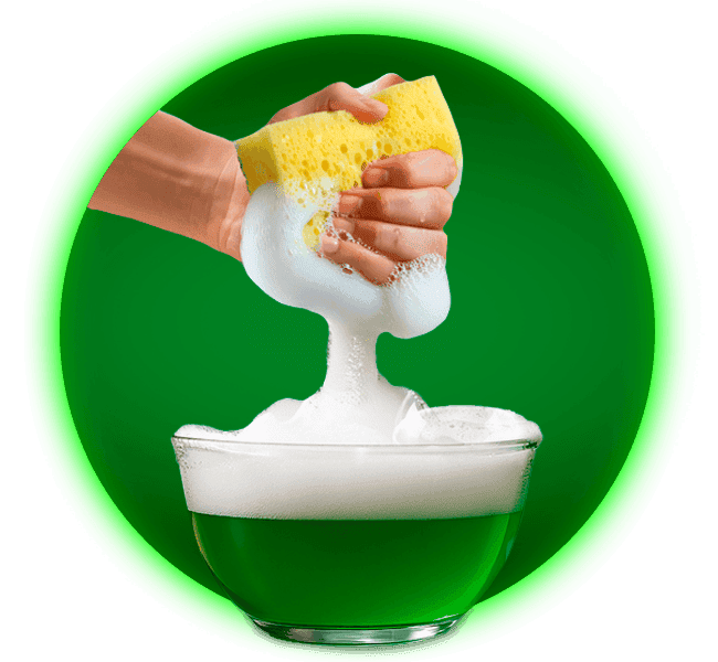 Mano exprimiendo esponja amarilla con potente espuma verde de Axion Limón en tazón de vidrio.