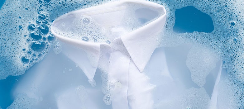 Camisa blanca sumergida en agua con detergente, siguiendo un proceso cuidadoso para evitar la formación de arrugas durante el lavado.