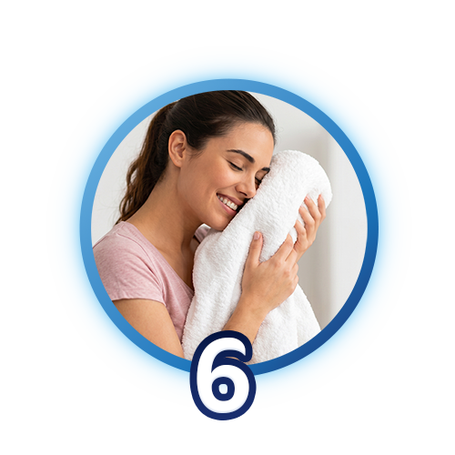 Paso 6: Mujer sonriente con los ojos cerrados abrazando una toalla blanca suave y recién lavada contra su mejilla.