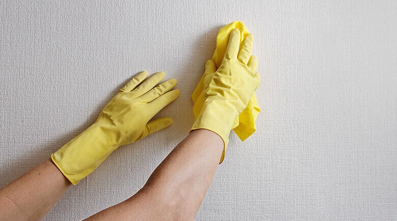 Imagen de manos con guantes amarillos limpiando la pared.