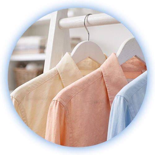 Hilera de camisas planchadas en tonos pasteles como rosa, azul y verde, colgadas ordenadamente en ganchos de ropa.