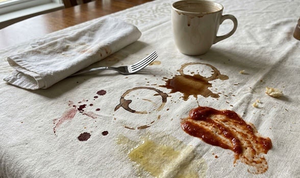 Mantel de tela blanco con manchas de café, vino y salsa sobre la mesa listo para el proceso de lavado de ropa.