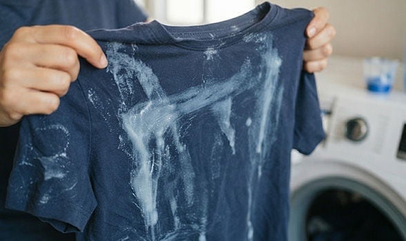 Persona sosteniendo una playera azul oscuro con residuos de detergente blanco por un mal enjuague al lavar la ropa.