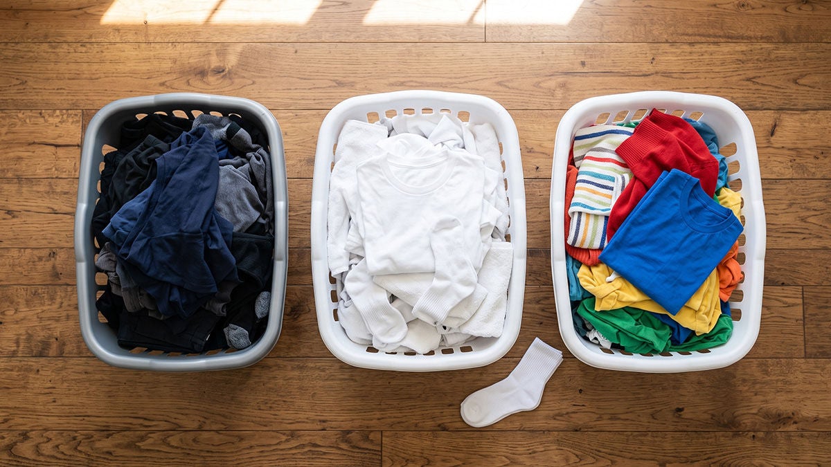 Cestas con prendas oscuras, blancas y de color, enseñando visualmente cómo lavar la ropa por colores.