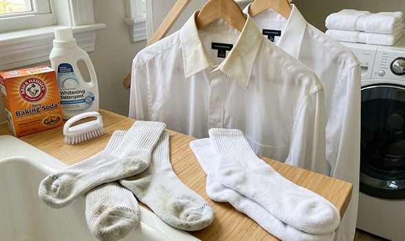 Bicarbonato de sodio, detergente y cepillo junto a prendas y calcetines blancos con manchas para lavar la ropa.