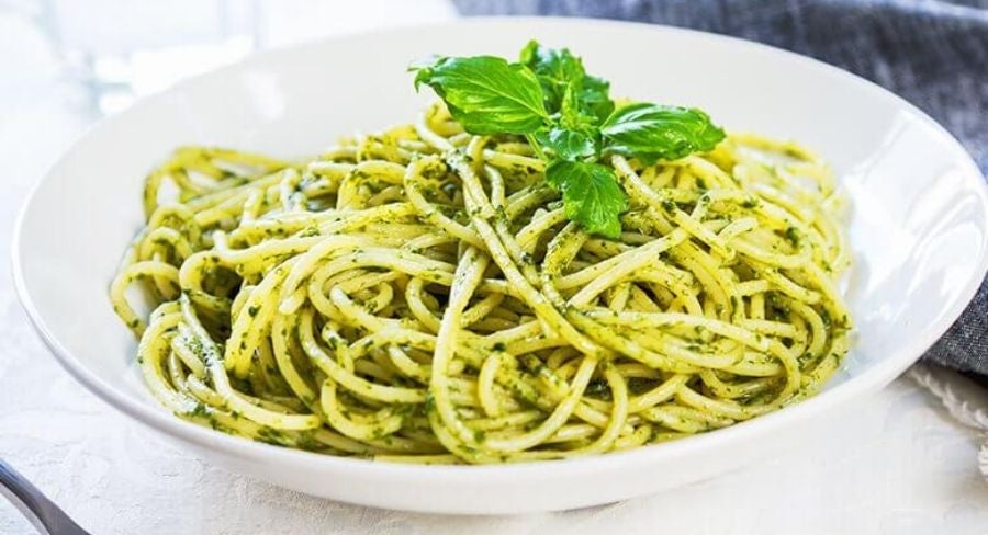Plato de espagueti verde decorado con hojas de perejil fresco, servido sobre un plato blanco