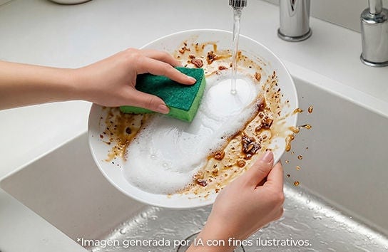 Manos lavando plato blanco con grasa y comida usando esponja verde bajo el agua del grifo en el fregadero