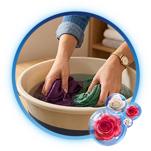Persona lavando prendas de color morado y verde a mano dentro de una cubeta de plástico con agua y suavizante diluido