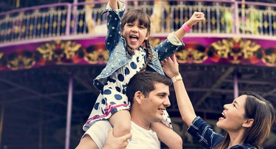 Padre cargando a su hija en hombro mientras visitan parque de diversiones