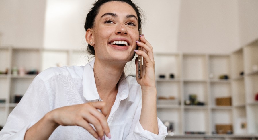 mujer sonriente desayunando y hablando por teléfono en casa