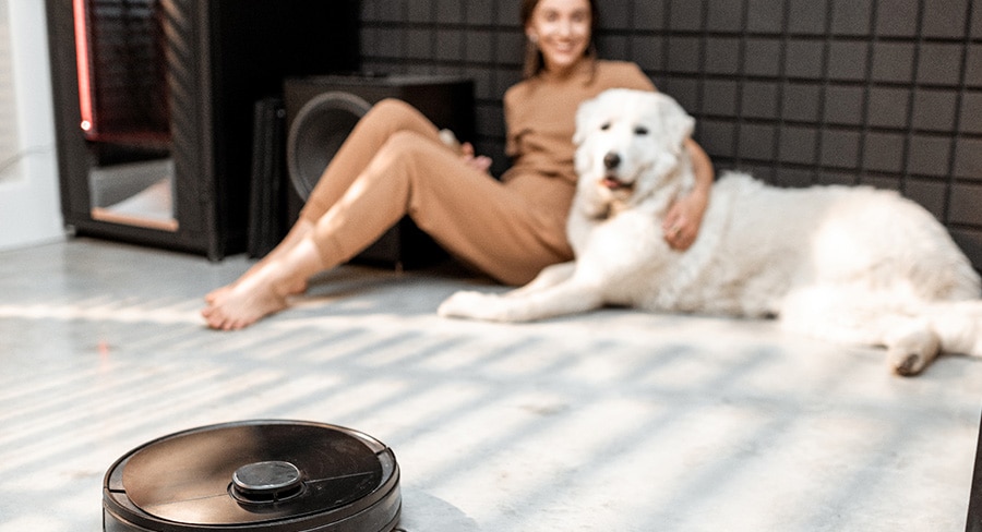 mujer sentada con su perro en cuarto mientras un robot barredor limpia el piso