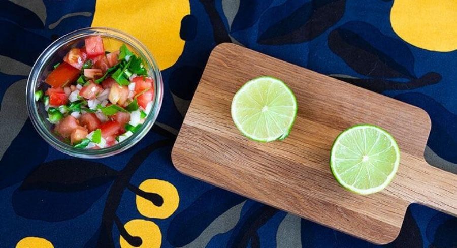 recipiente con pico de gallo, tabla de madera y limones picados