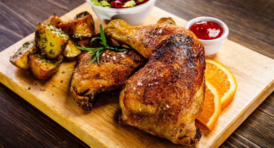 piezas de pollo cocinadas a la parrilla con papa al horno y ensalada de verduras sobre mesa de madera